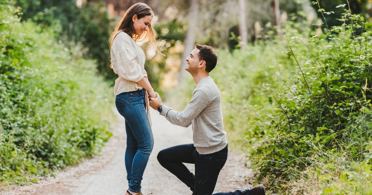 Man proposing on one knee to a woman on a dirt path in the forest