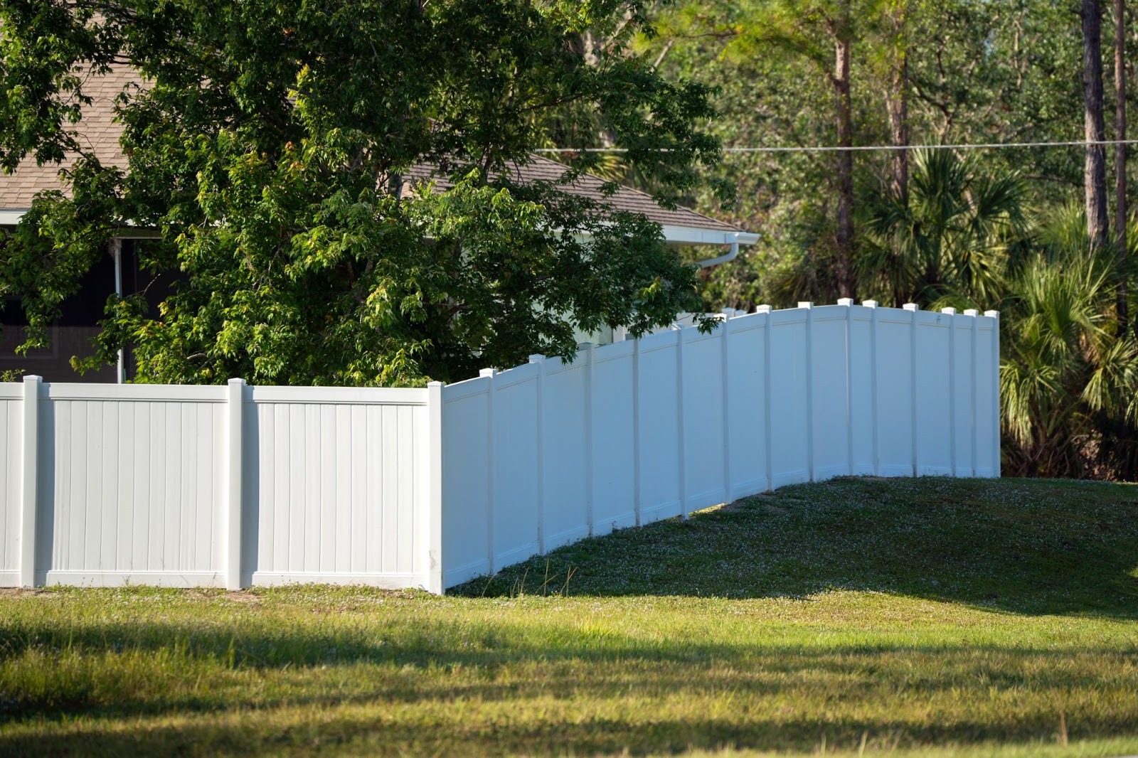 Vinyl fence around a home next to grass and trees. 