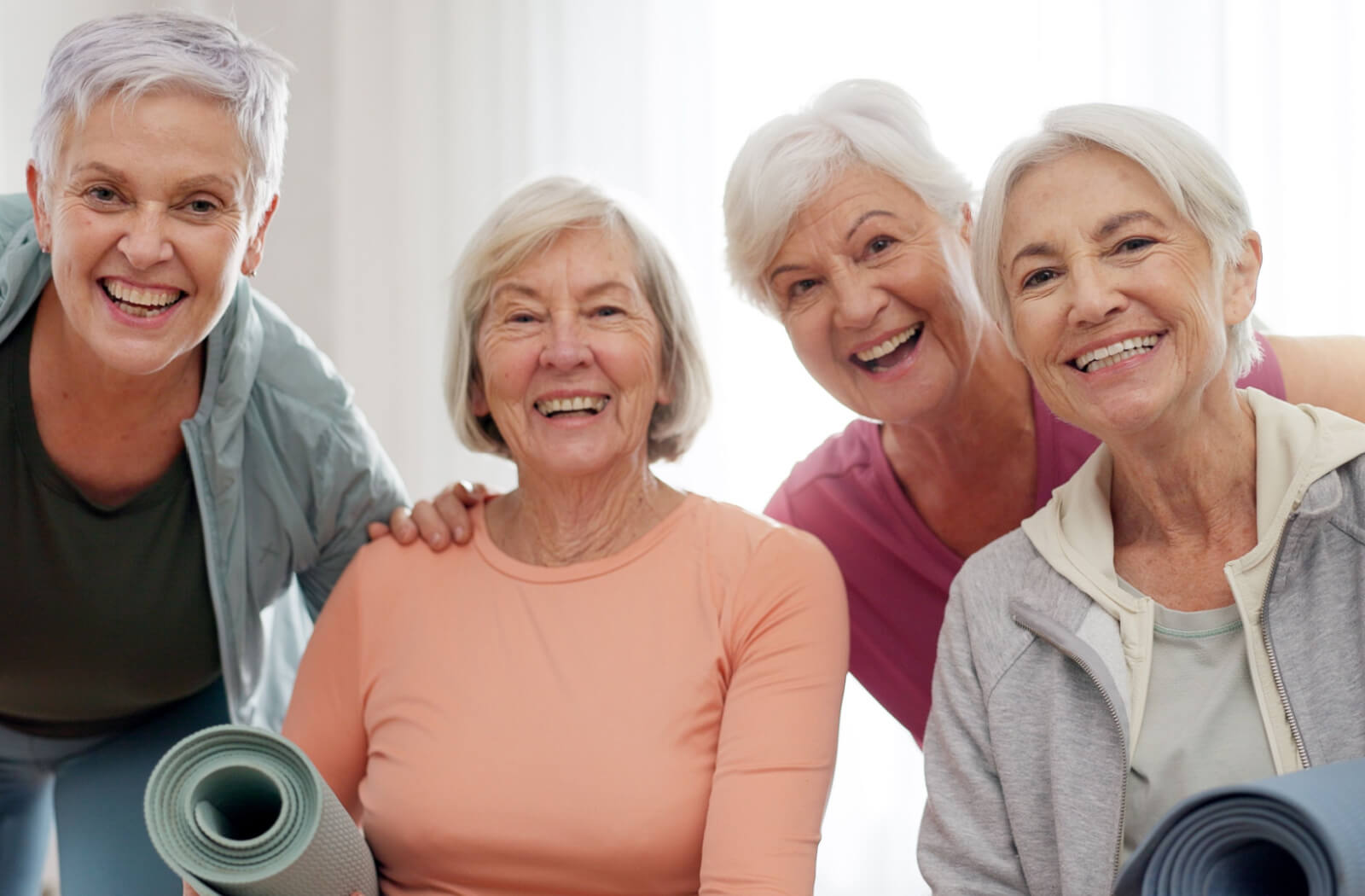 A group of older adults smiling at the camera and holding yoga mats after a fitness hobby class for seniors.