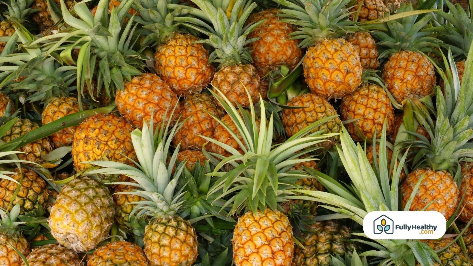Fresh pineapples piled together with leafy tops and golden-orange skins