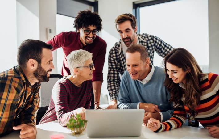 Six employees working together while looking at a laptop on a desk.