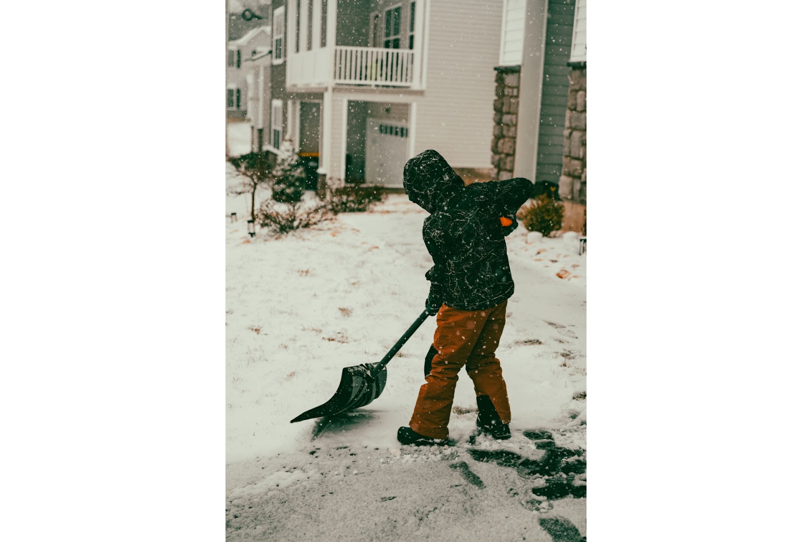 A young boy with a snow shovel in the snow.