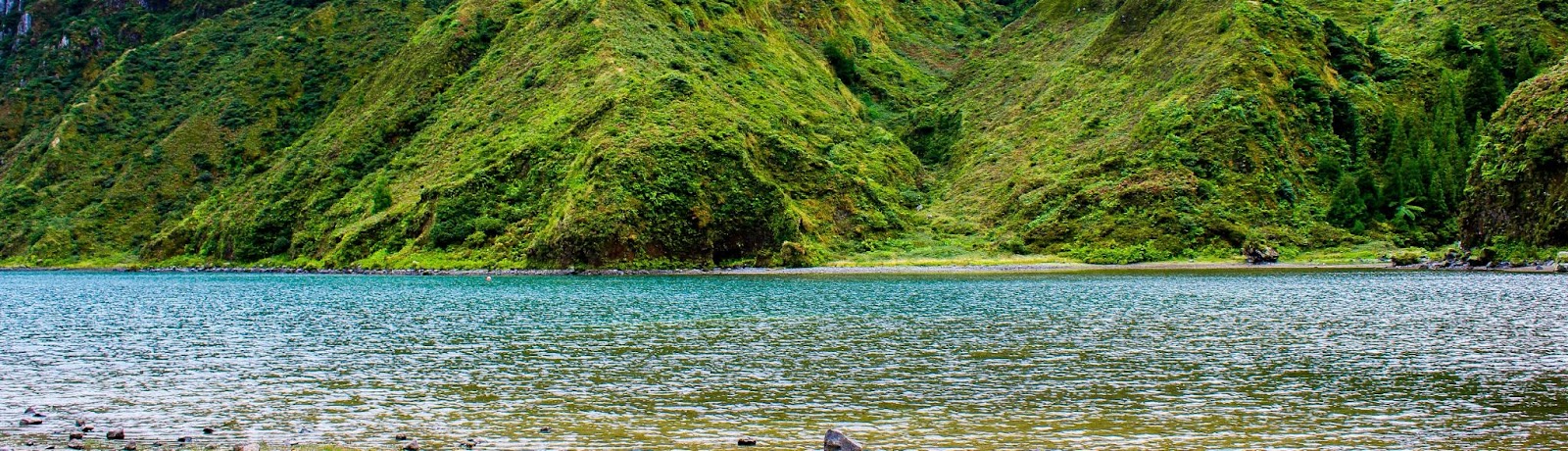 Lagoa cercada por montanhas verdes cobertas por vegetação densa, representando a natureza exuberante de onde fica a Ilha de São Miguel, em Portugal.