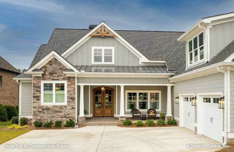Front exterior view with stone and cedar shake siding, covered entry porch, and a side-loading garage topped with a large shed dormer.