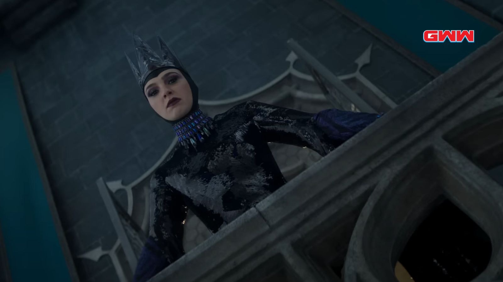 Gal Gadot as the Evil Queen, looking down from a balcony, wearing a crown.