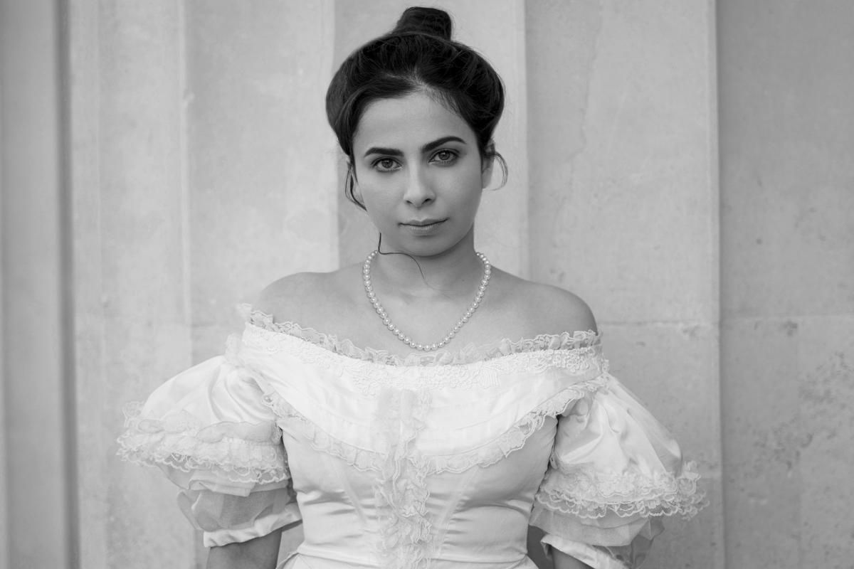 A blac and white photo of a woman wearing an off-shoulder white dress.