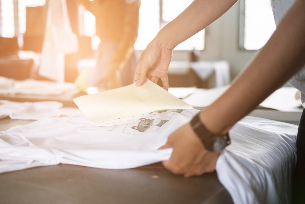 A person peeling the paper from waterproof film on a custom T-shirt as part of the DTF printing process.