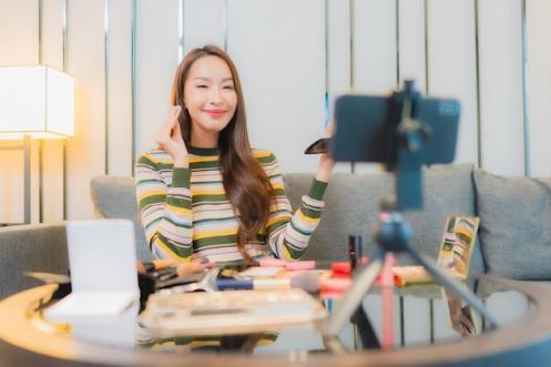 Portrait of beautiful young asian woman reviews and uses cosmetics on sofa