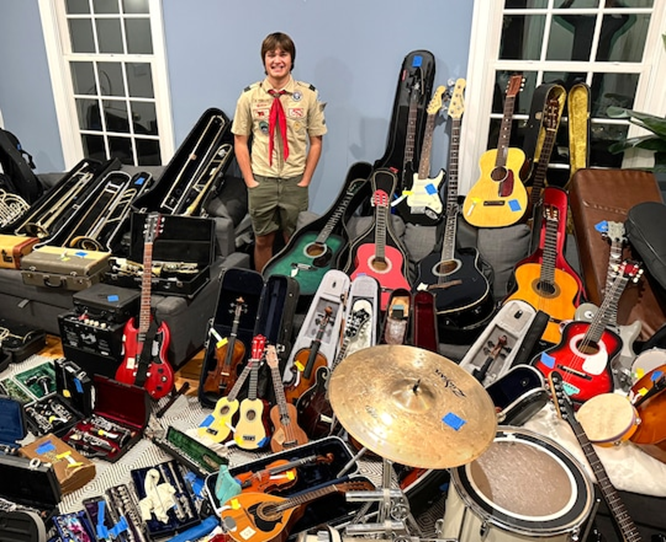 Picture of a high school student in a boy scout uniform next to several instruments he collected as part of a service project.