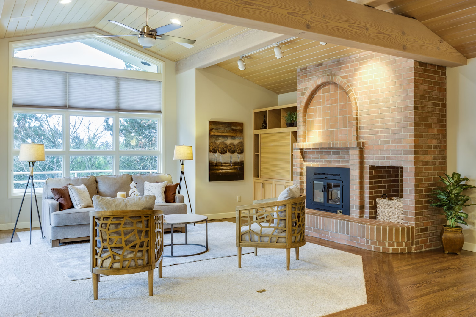 This image depicts a cozy living room with large windows looking out to a woodsy landscape. 