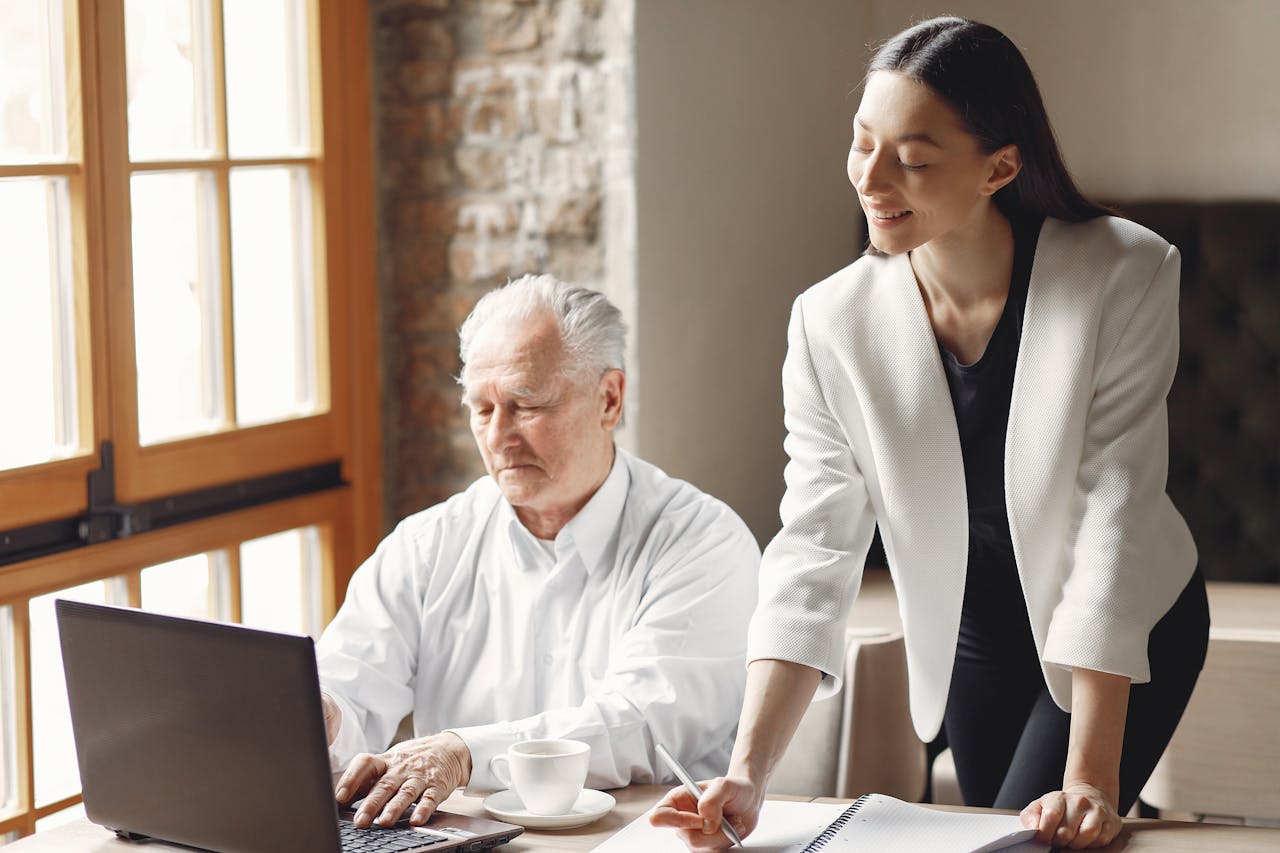 A woman and an older man sitting side by side, working intently on a laptop, sharing ideas and insights.