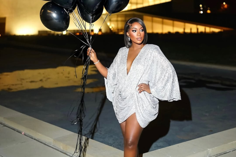 A woman in a silver satin birthday dress with black balloons.