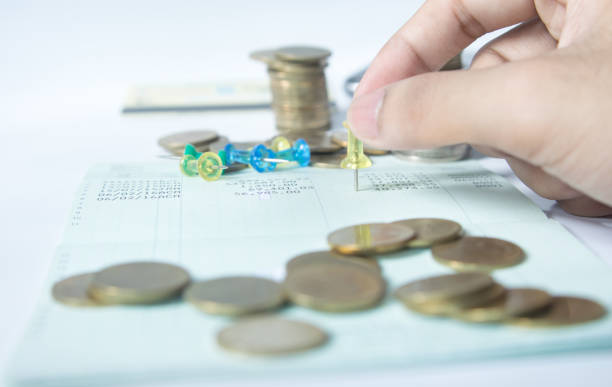 Somebody holding a thumb tack over a piece of paper that has coins on it.