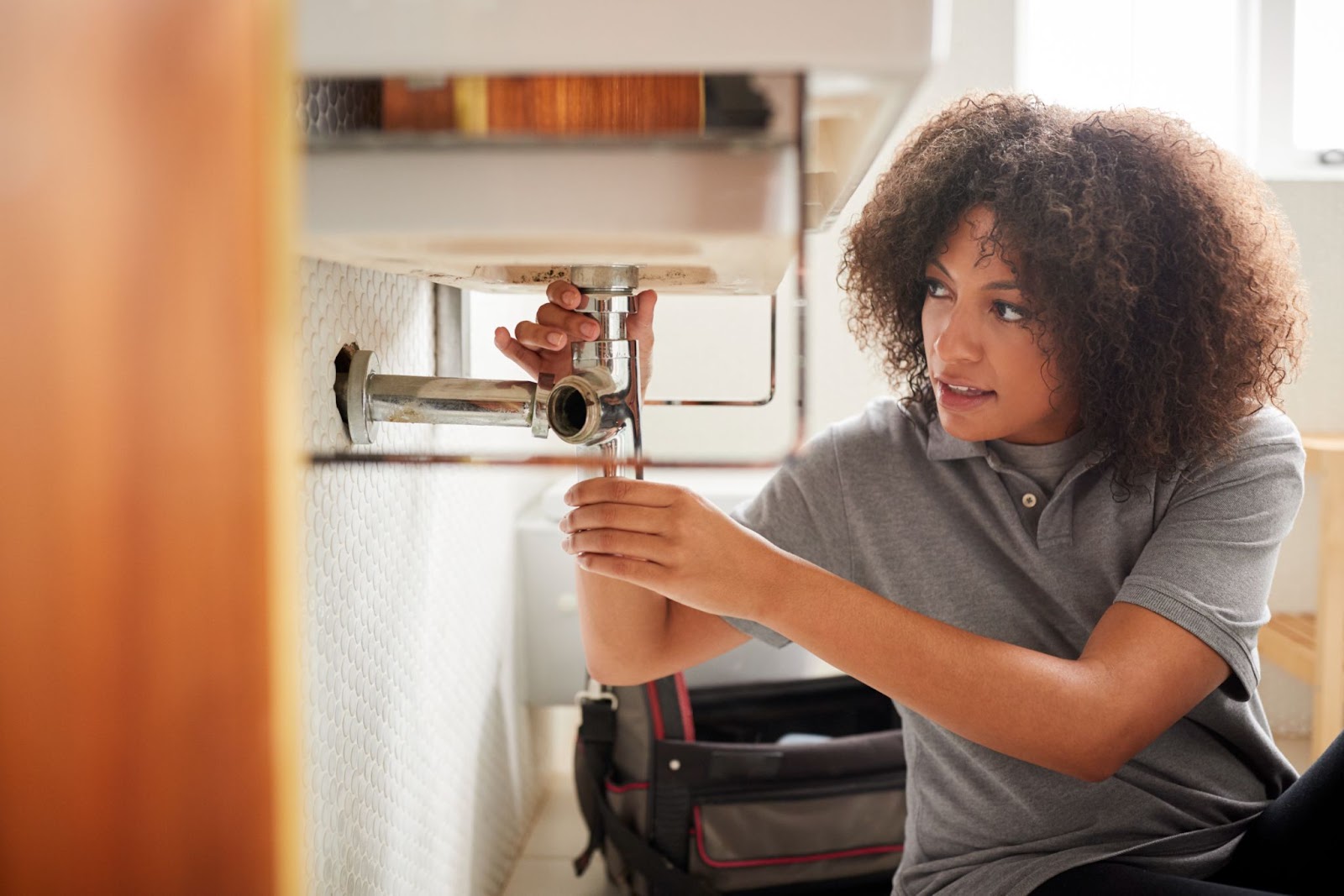 A female plumber on the floor is fixing the bathroom sink.