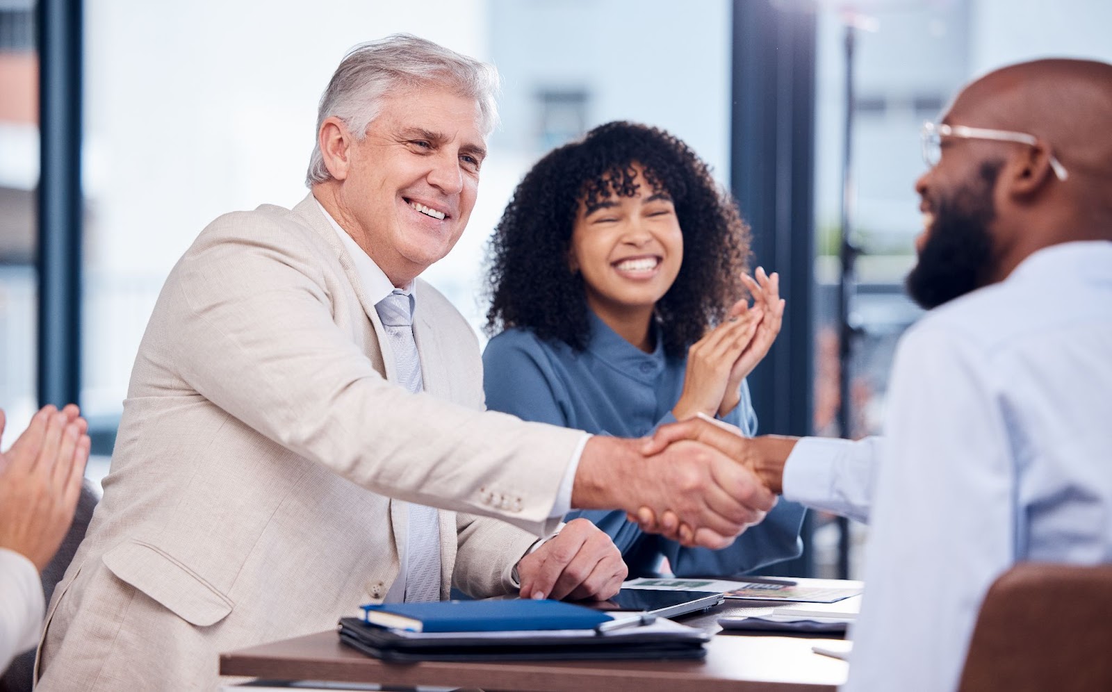 Two men shaking hands next to a smiling woman. 