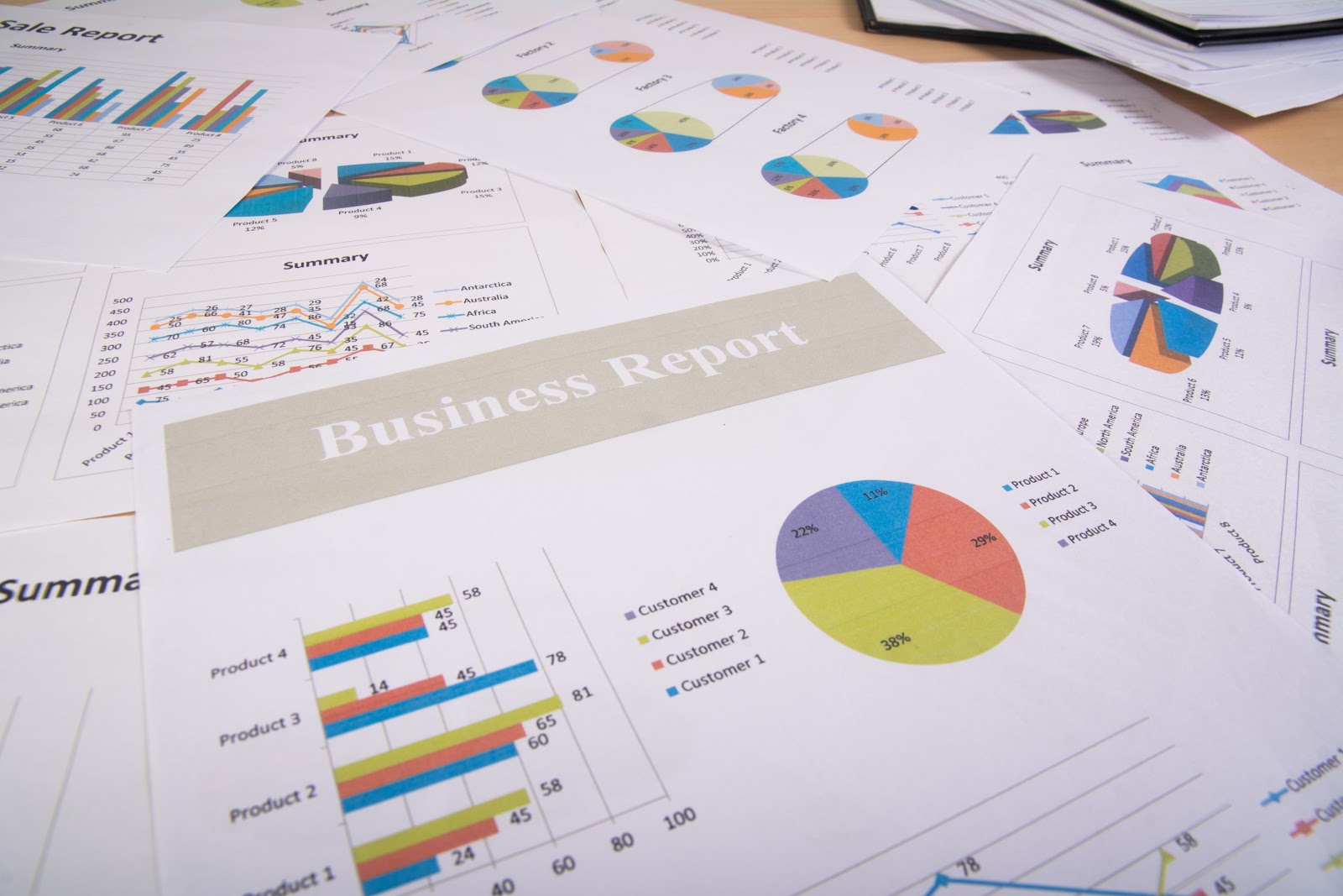 A collection of printed business reports showing various financial data, sales data, and pie charts used in enterprise reporting and ad hoc reports.