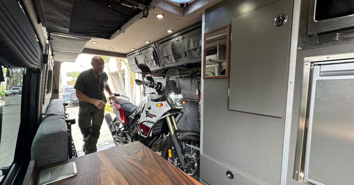 a guy walking through his campervan with a dirt bike inside 