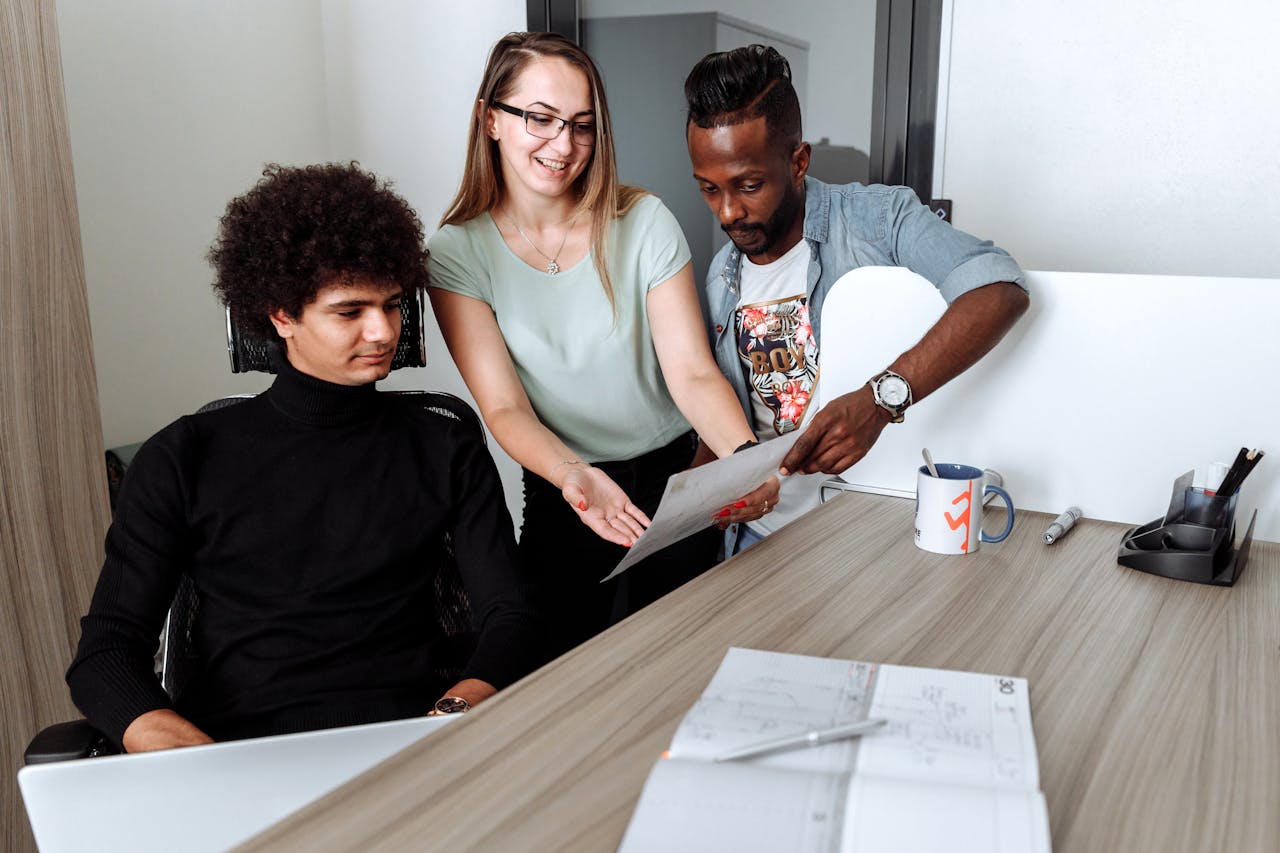 Three colleagues collaborating in an office, reviewing documents and discussing strategies, illustrating teamwork to manage small business efficiently.