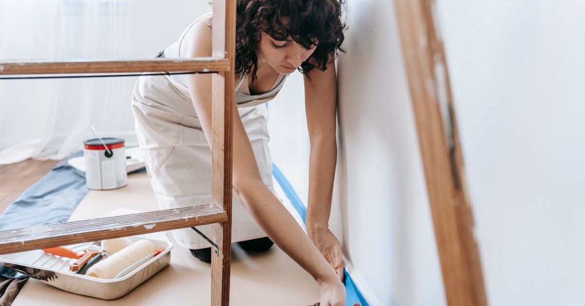 Woman uses tape to prep wall for painting, part of a DIY home renovation project indoors.