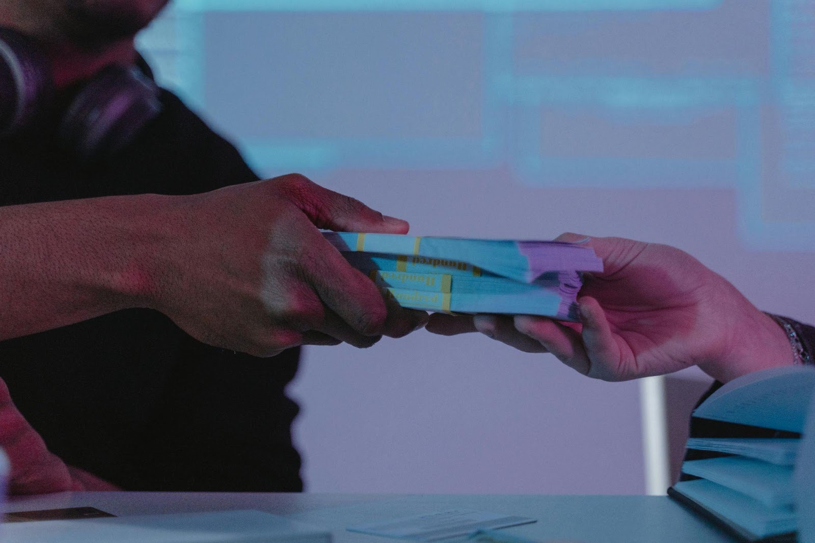 [wo people exchanging a stack of cash in a low-light setting, focusing on the hands passing the money]