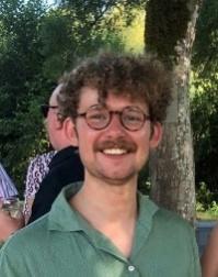 A person with curly hair and glasses smilingDescription automatically generated