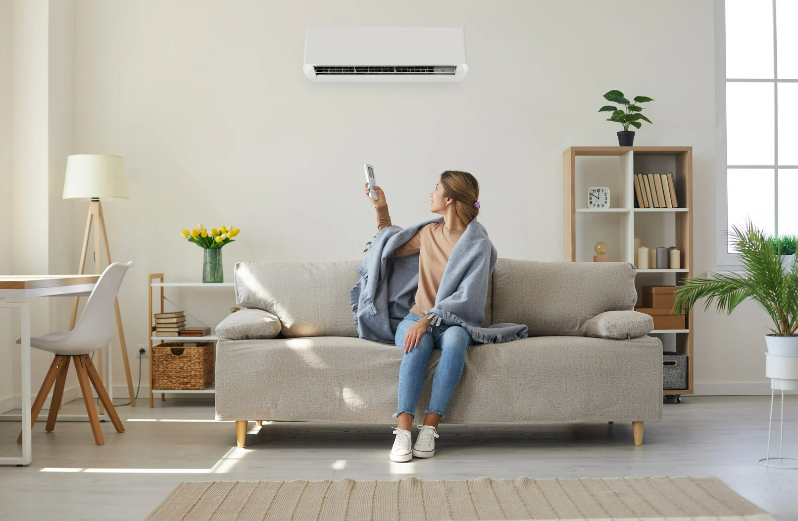 Woman turning on hvac system while covered in blanket