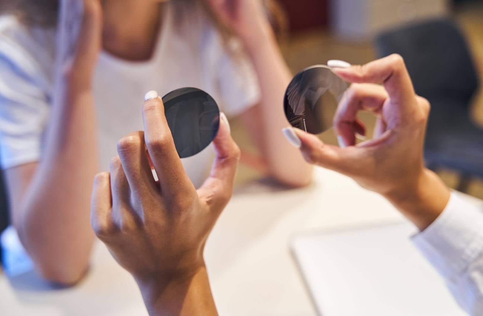 An optician holds two lenses (polarized and non-polarized) side by side, to explain to a patient that you cannot always tell them apart by looks alone.
