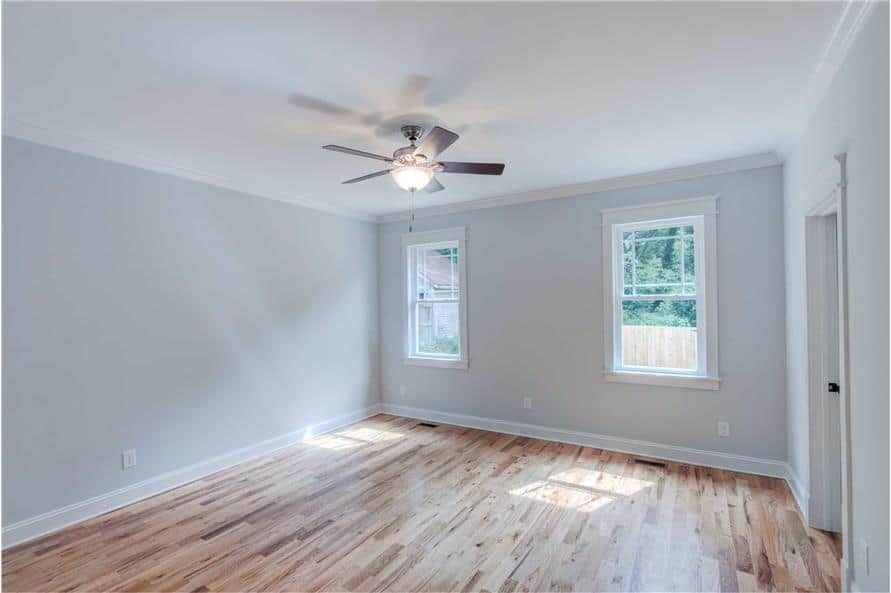 Primary bedroom with hardwood flooring, gray walls, and a couple of white-framed windows.