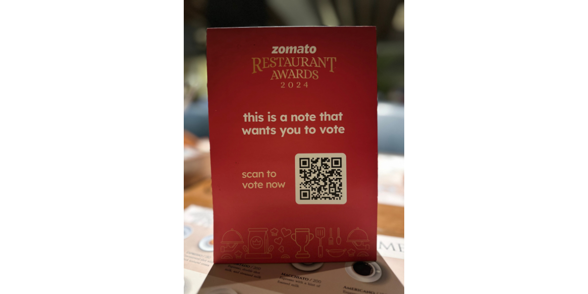 A table tent with Zomato Restaurant rewards QR Code, asking people to scan and vote for their favorite restaurants.