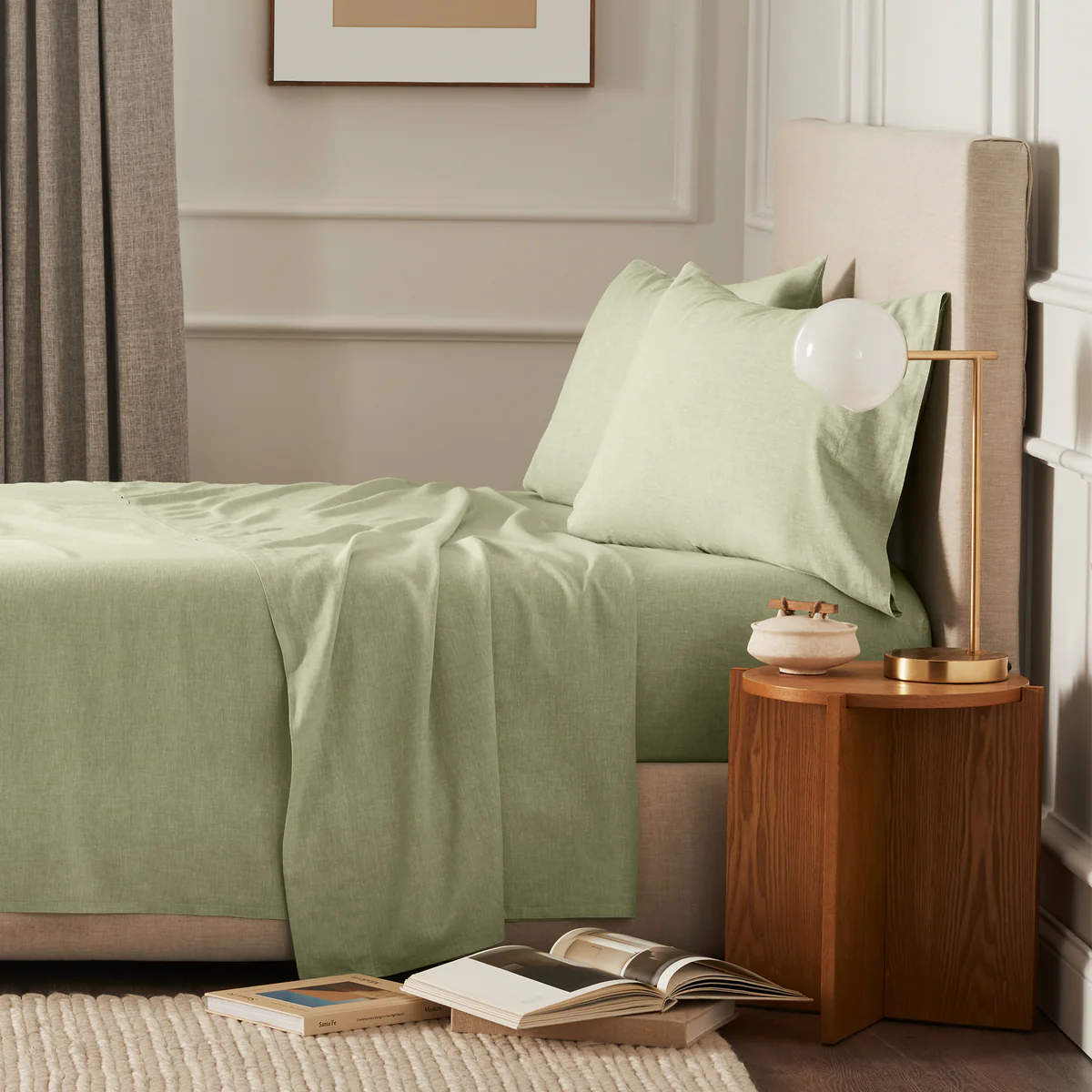 A bed with light green sheets and pillows, a nude headboard, and a wooden nightstand next to it