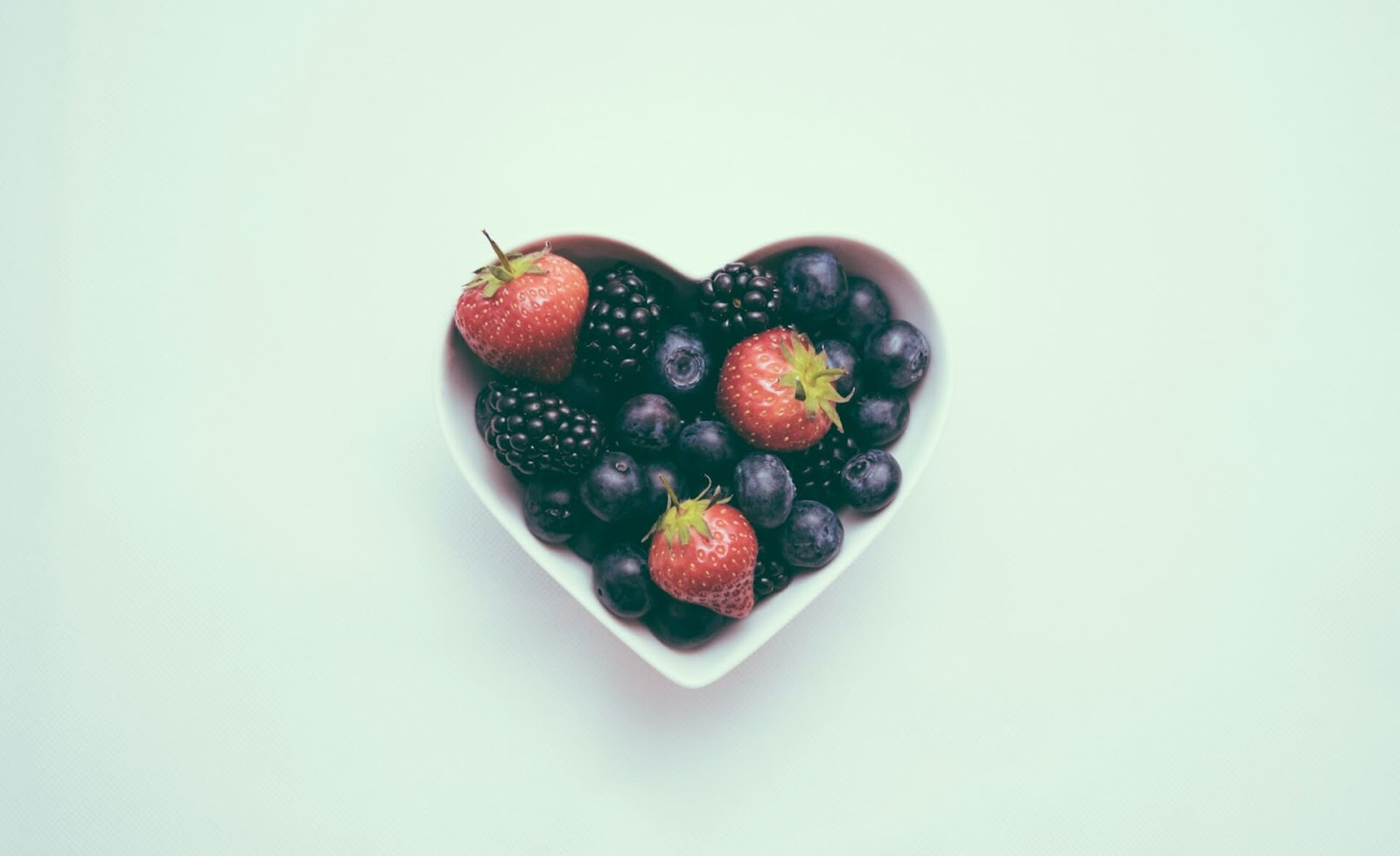 A heart-shaped bowl filled with assorted berries, including strawberries, blackberries, and blueberries, symbolizing the nutrient-rich elements in an ADHD smoothie.