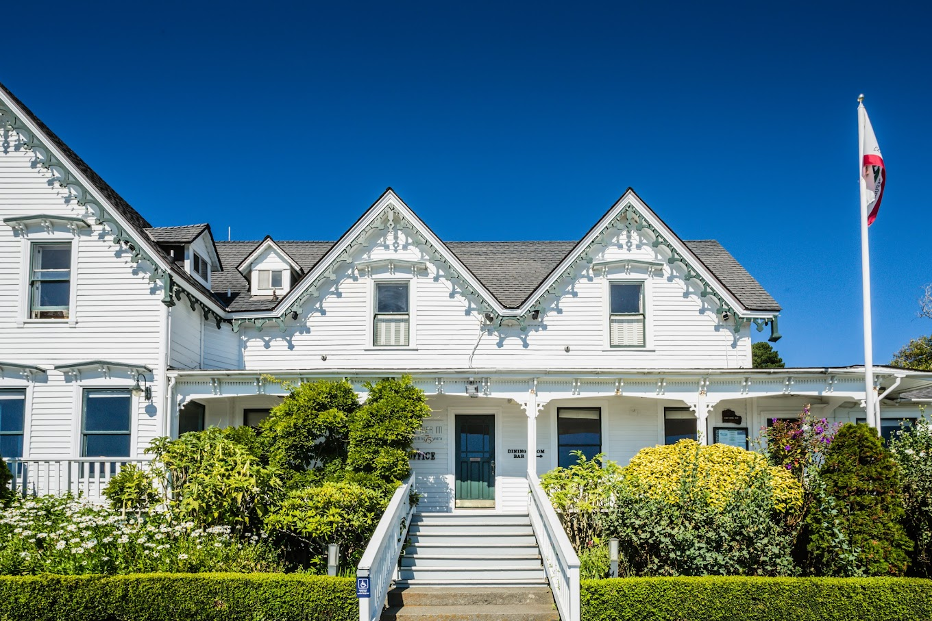 A charming white colonial-style 3 star hotel surrounded by lush greenery under a clear blue sky, offering the allure of one of the top secret stays in California, perfect for a peaceful and picturesque retreat.