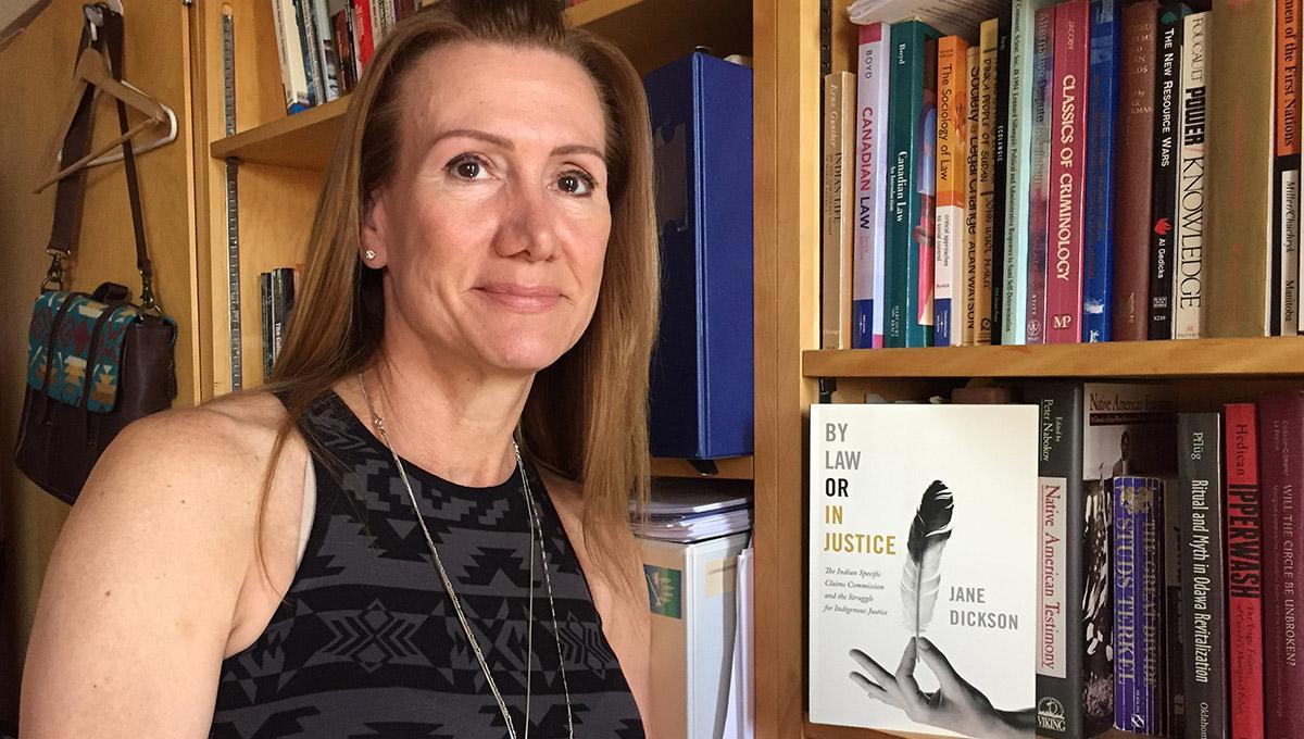 A picture of Jane Dickson, a law professor at Carleton University. She poses beside her book called "By Law or In Justice". 