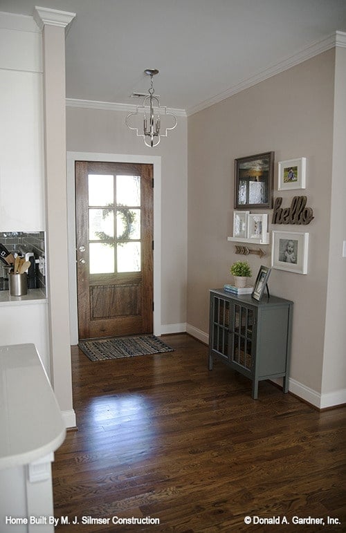 Foyer with a wooden glazed entry door, a chrome pendant light, and a console table topped with gallery frames.