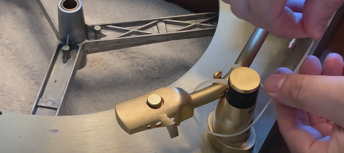 Hands securing the tonearm of a vintage turntable with a zip tie for safe handling.