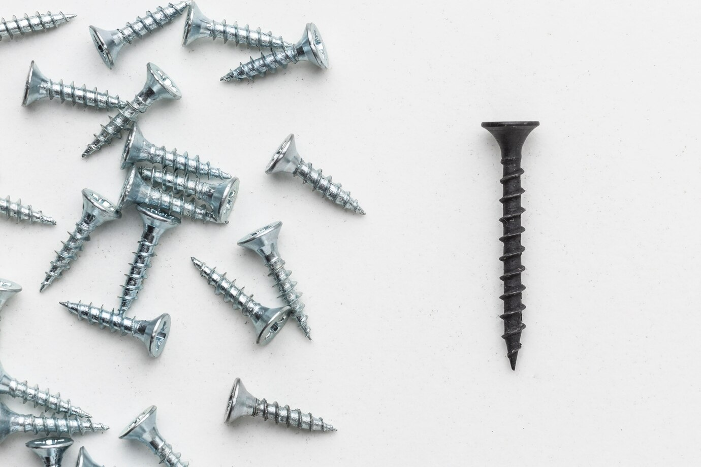 A collection of shiny silver screws for Garage Doors scattered on a white surface, with a single black screw standing out to the right, emphasizing contrast in design and purpose