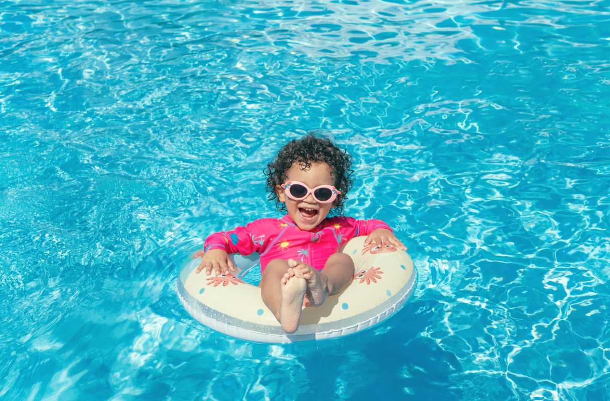  A smiling little girl in sunglasses enjoys the swimming pool in an inflatable float.