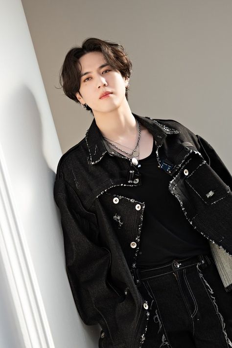 This contains an image of GOT7's Yugyeom leaning against a wall wearing a black denim jacket and silver chain necklace