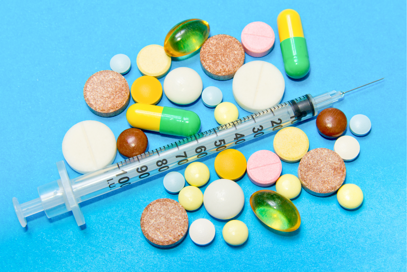 Different pills and a syringe laid out on a blue surface