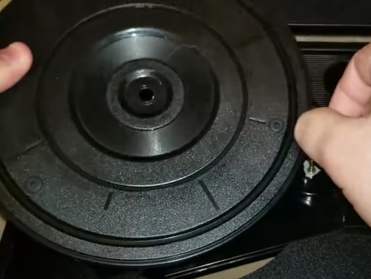 A person holding a turntable's platter during maintenance or assembly.