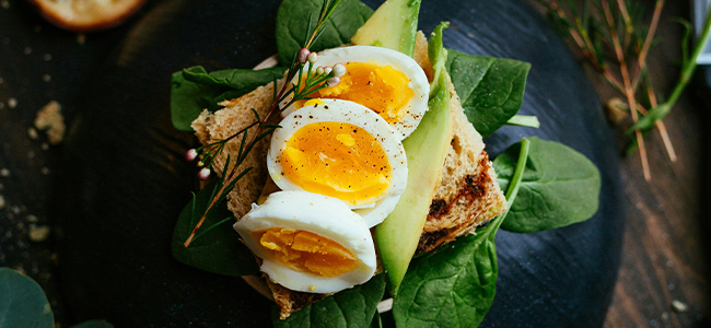 Toast topped with sliced medium-boiled eggs, avocado, fresh spinach, and herbs.