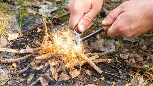 A camper gathers some grasses and wood lighting it up with a flint and steel method as a technique on  how to start a fire without matches or lighters
