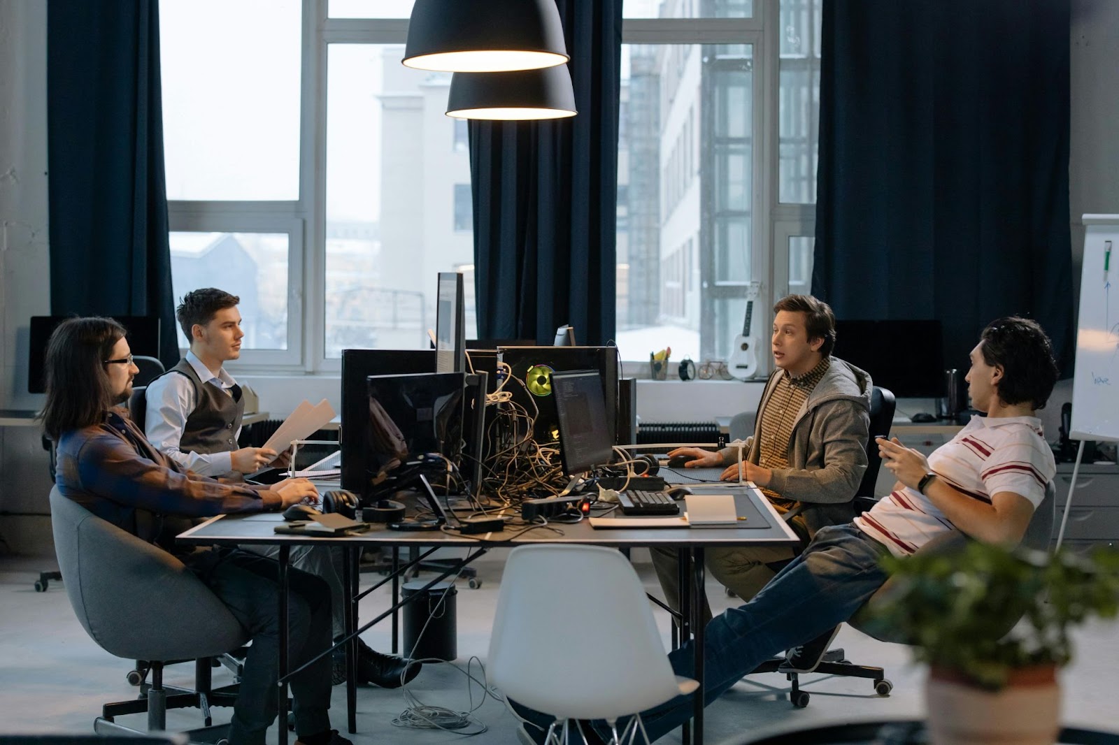 Four people work together in an office, seated around a table with computers and monitors.