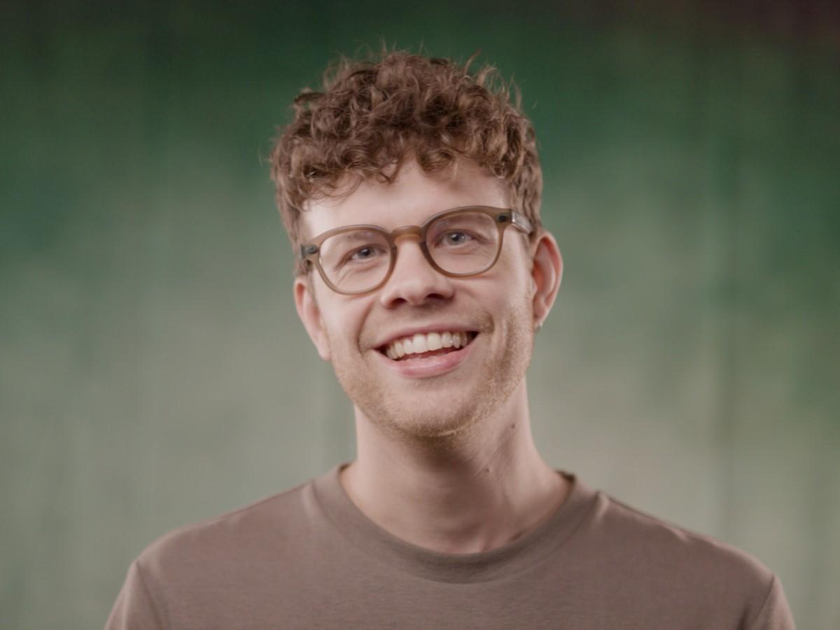 Dr Simon Ruffell in a brown t-shirt and brown glasses, smiling at the camera.