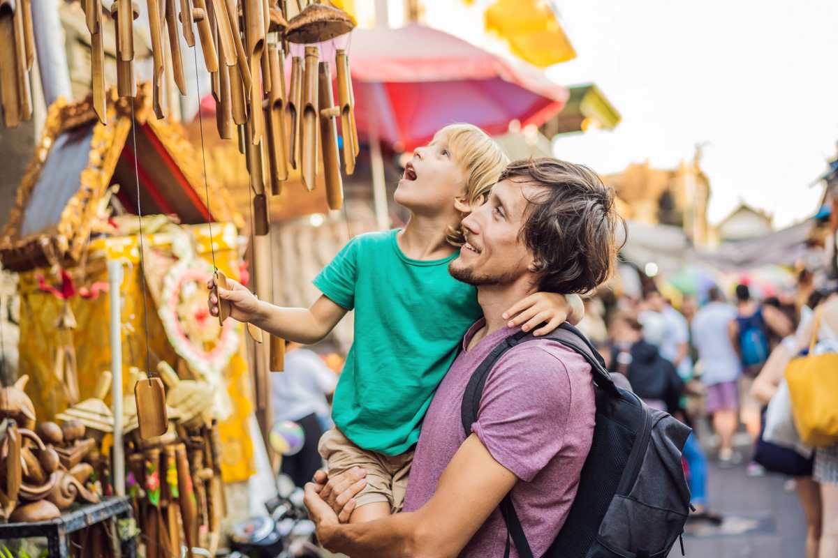 A father and son admire a walk of goods for sale at a festival.