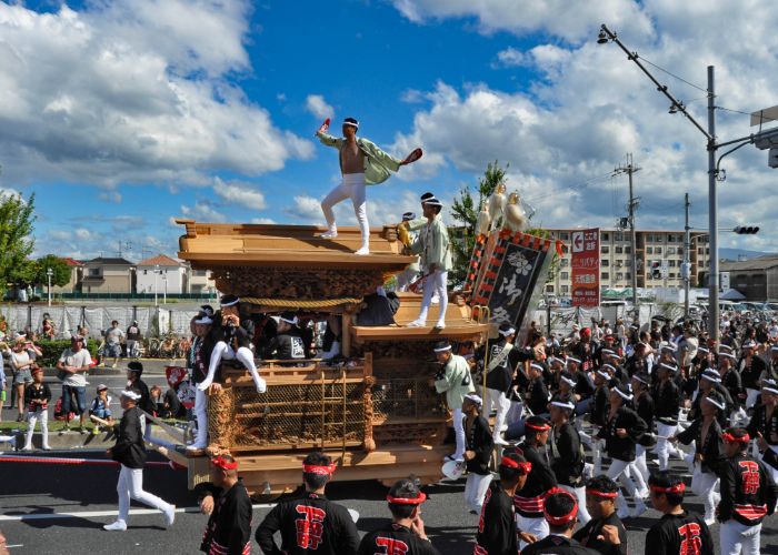 A festival float parading through the streets while one man stands on top of the float during the Kishiwada Danjiri Matsuri in Osaka