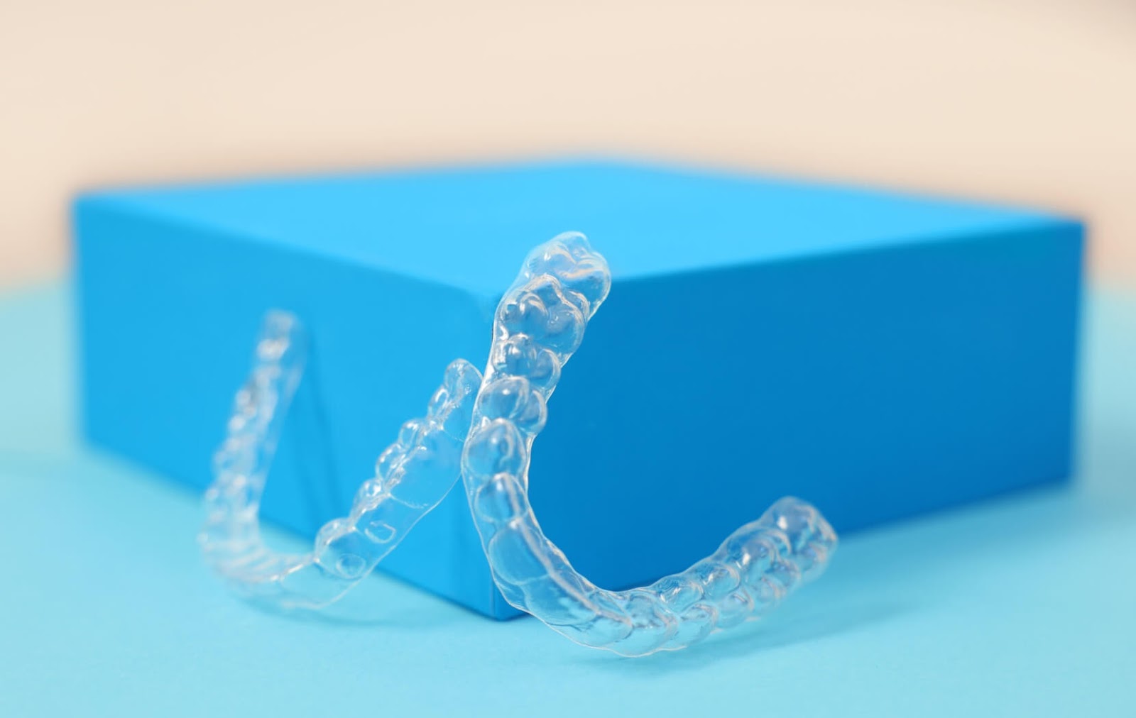 A pair of clean, new Invisalign aligners sit propped up against a blue block, ready for use.
