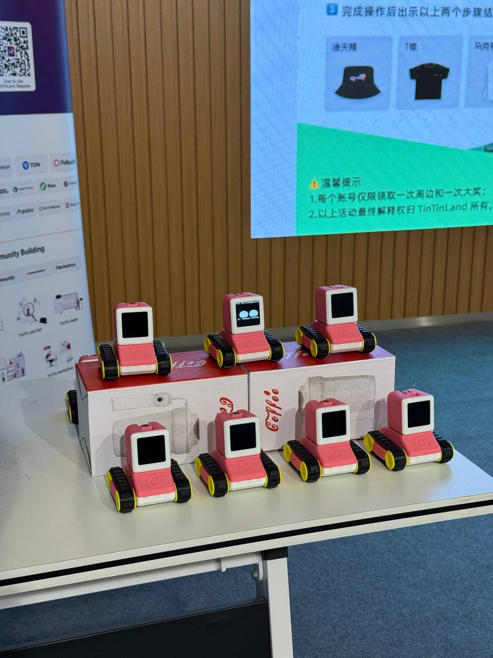 On display: Seven pink and white cuboid robots on wheels, each with a square screen resembling a TV for a face.