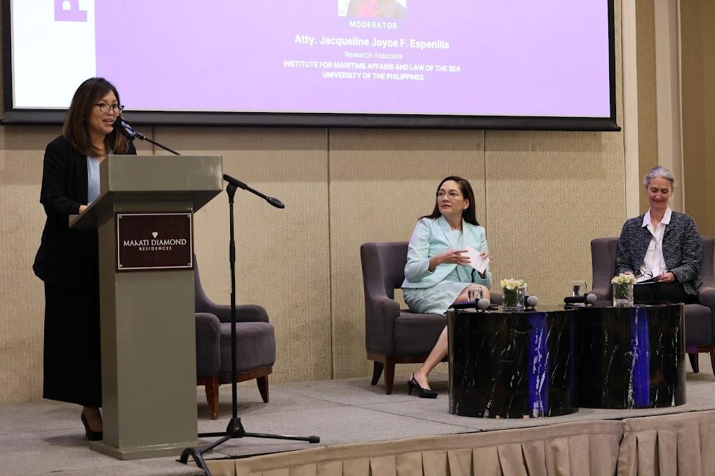 A person sitting at a podium with a microphone and a person sitting at a podiumDescription automatically generated