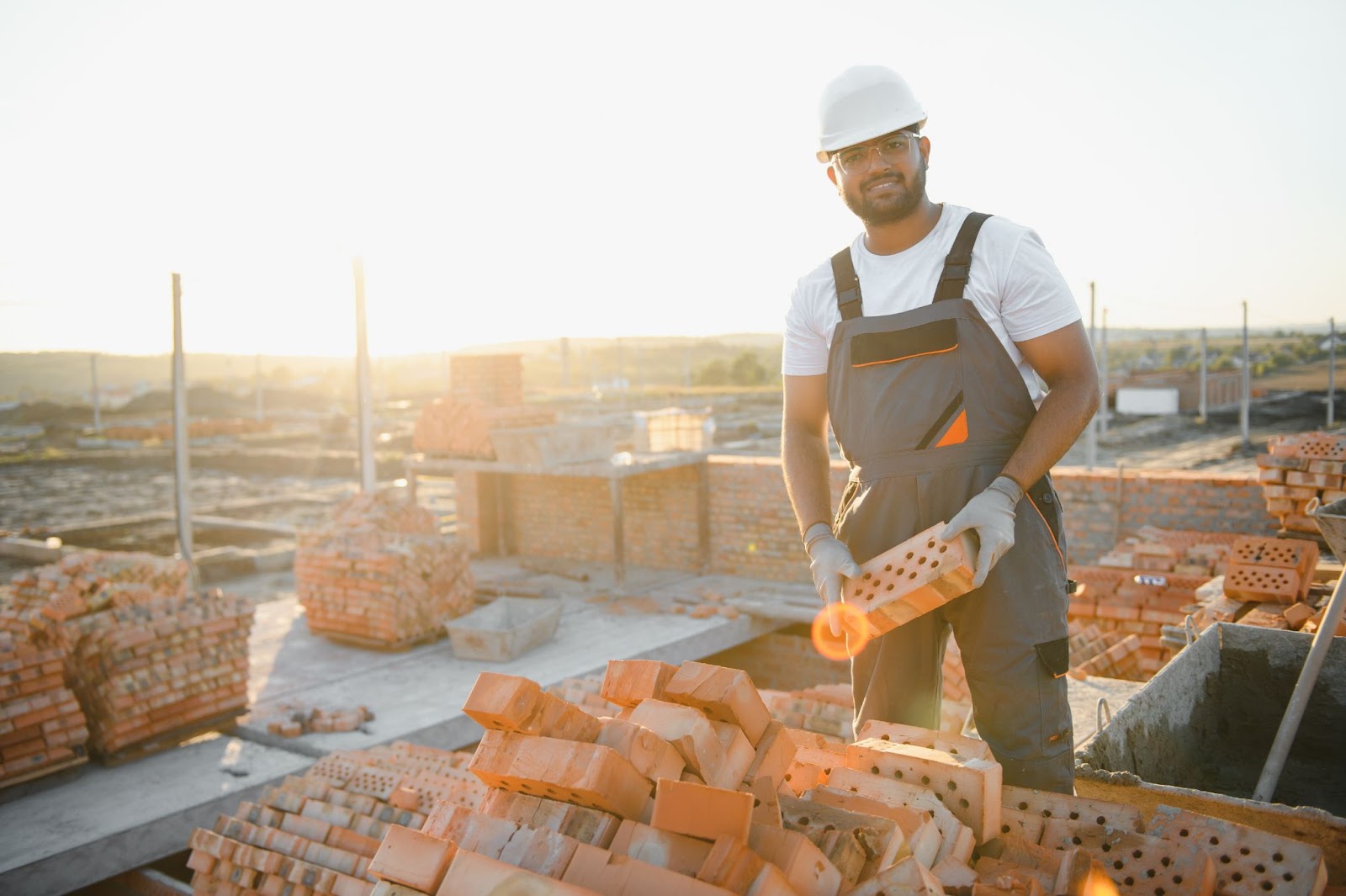 A construction worker in overalls checks the bricks for quality before use in building work.